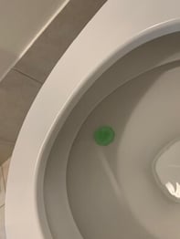 A toilet bowl with a green cleaning tablet dissolving in the water, indicating active cleaning and freshening.