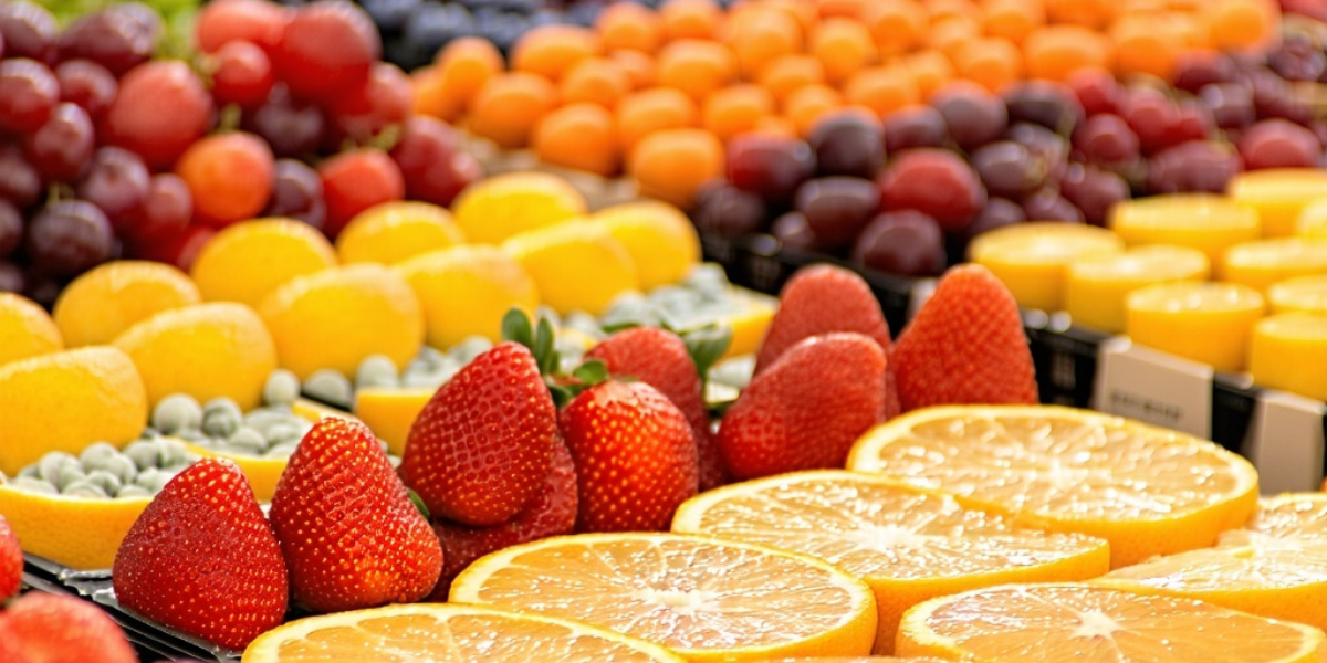 Colorful assortment of fresh fruits including sliced oranges, strawberries, grapes, and berries displayed neatly in rows. The vibrant, hygienic presentation highlights freshness, quality control, and food safety practices aligned with ISO 22000 standards in handling and preparation.